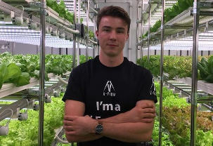 Hombre posando orgulloso con cultivos verticales de fondo.